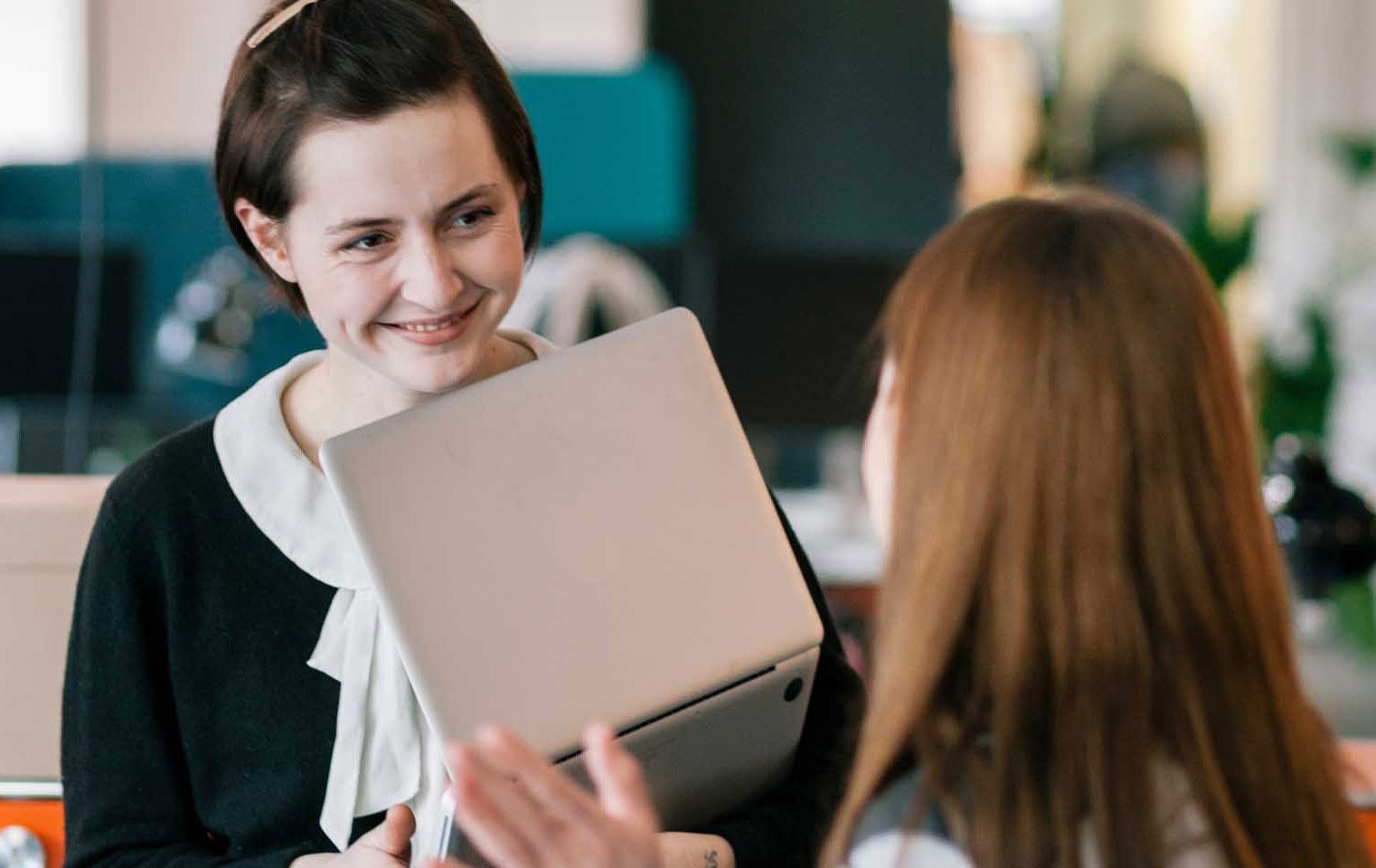 Happy young professional with a laptop in her hand, talking to another person